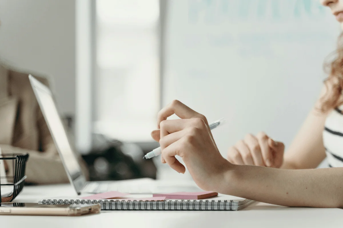 Closeup of a hand holding a pen and using a laptop computer.