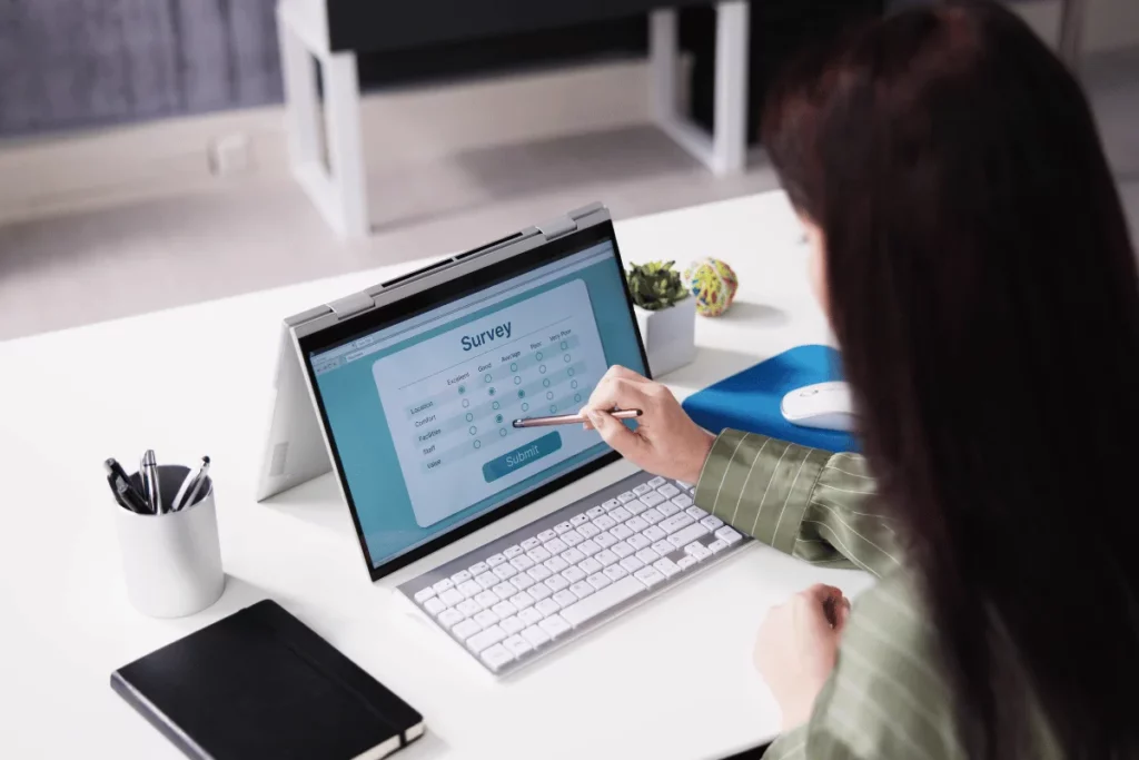 Person writing in a notebook beside a MacBook with a search page open.