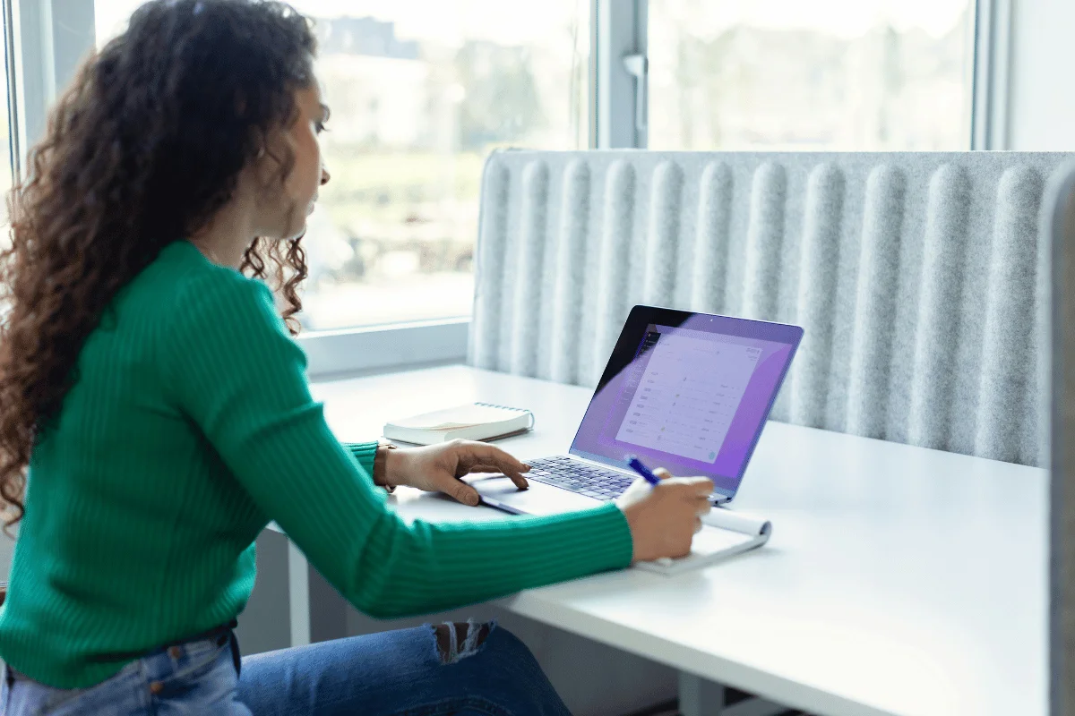 Woman in green sweater working on laptop at desk.
