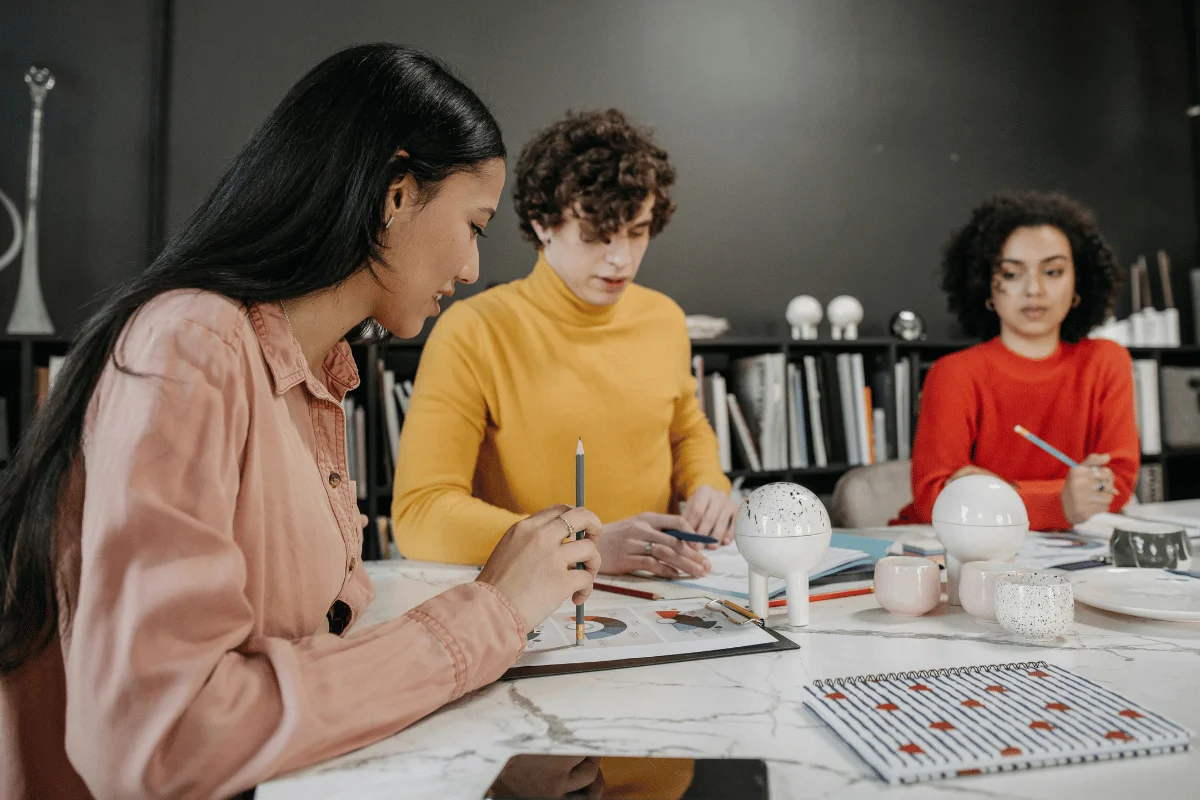 Three people at a table with painting supplies, focused on an art project.