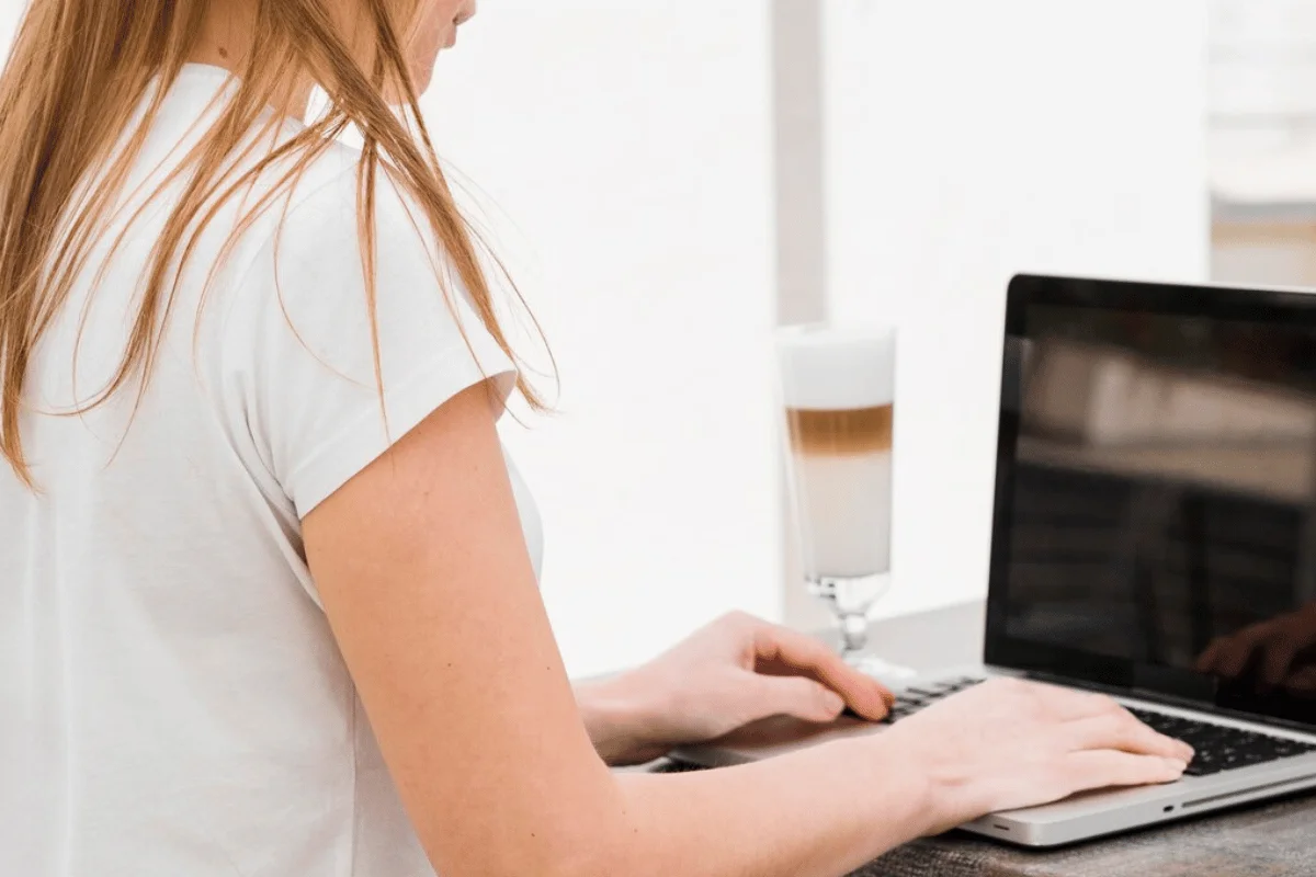 A woman typing on a laptop computer, focused on the screen with a cup of coffee beside her.