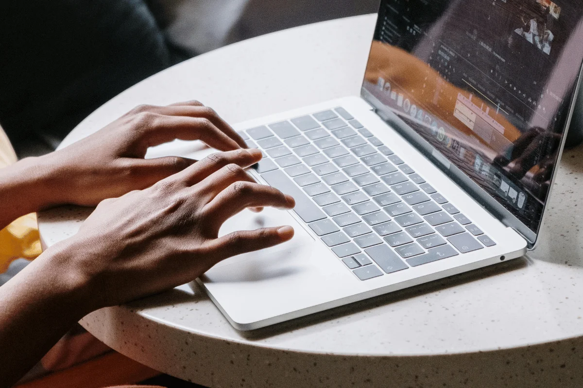 Individual editing a video on a laptop, with hands typing on the keyboard, placed on a white round table.