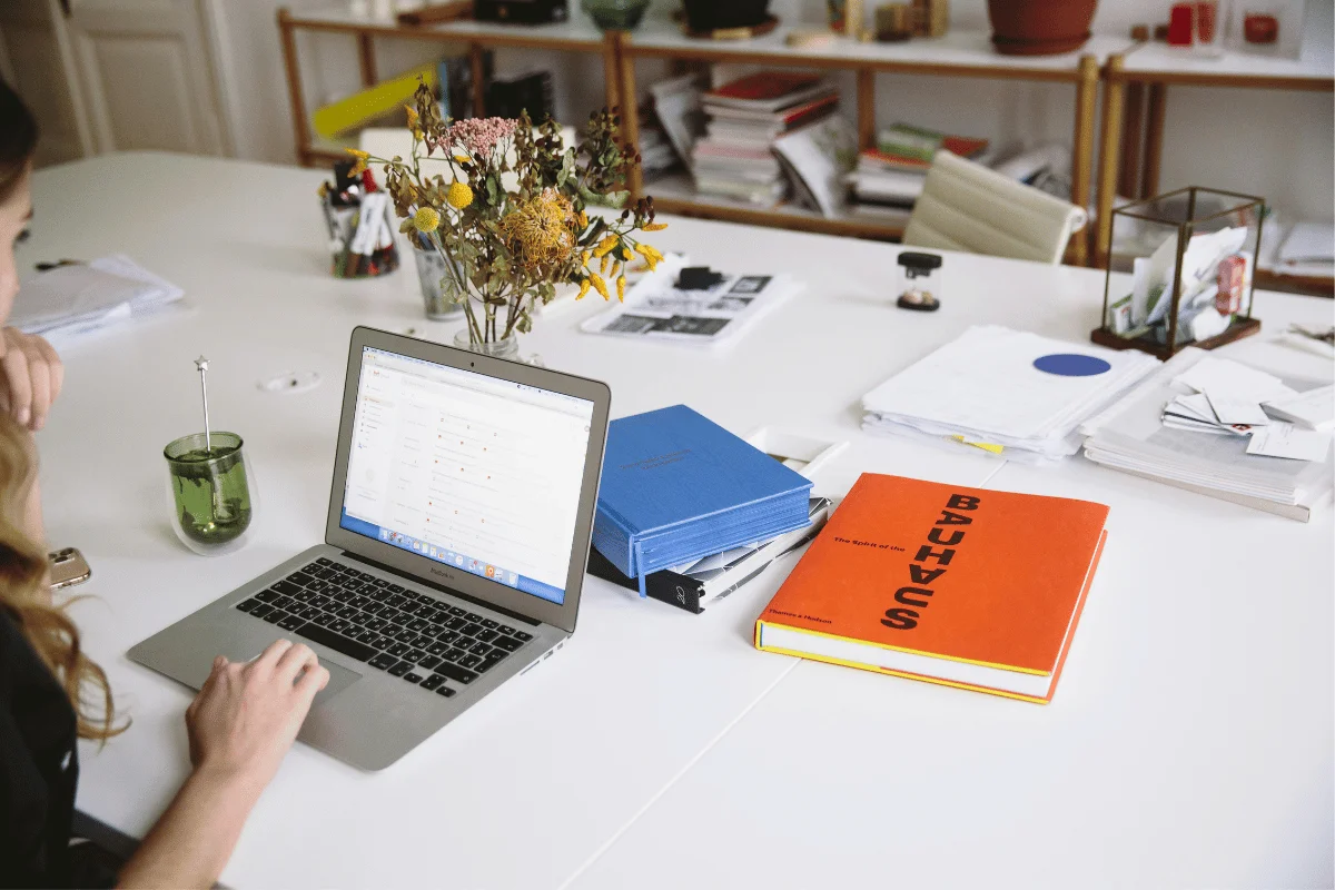 Woman working on a laptop at a white desk with office supplies.