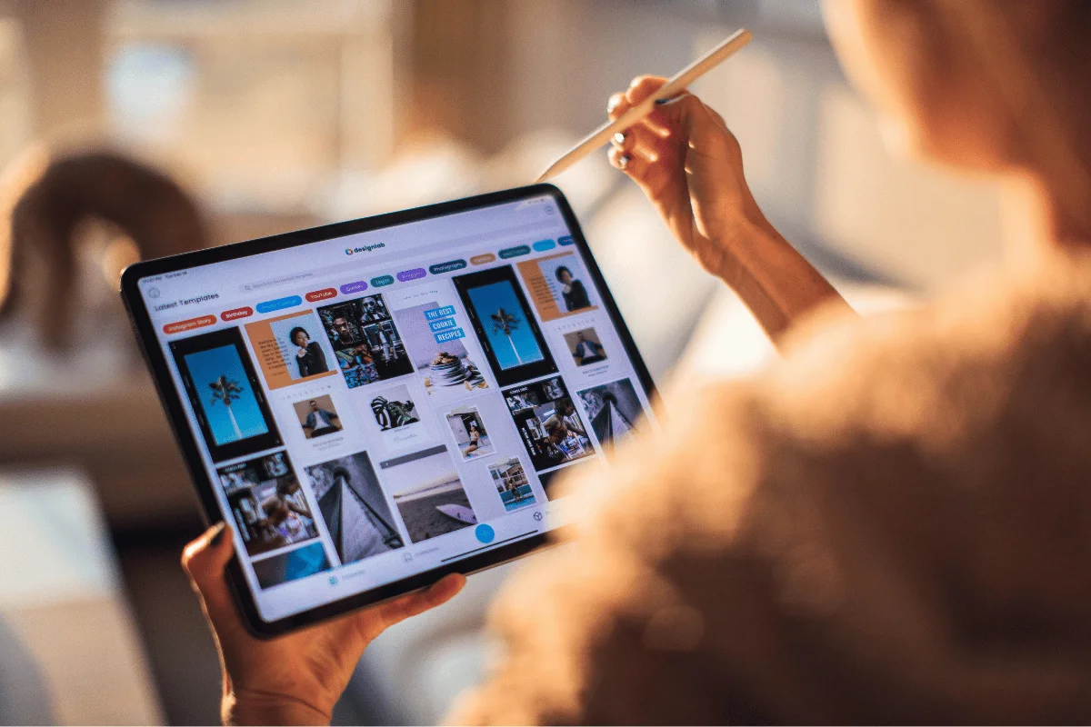Close-up of a person holding a tablet and stylus, browsing through design templates in a well-lit living room.