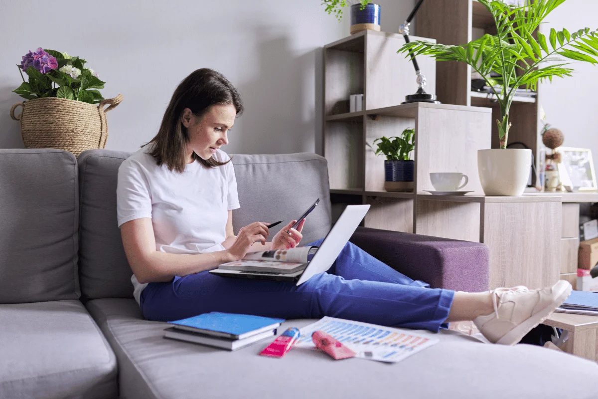 Woman working from home on a laptop, checking her phone for information.