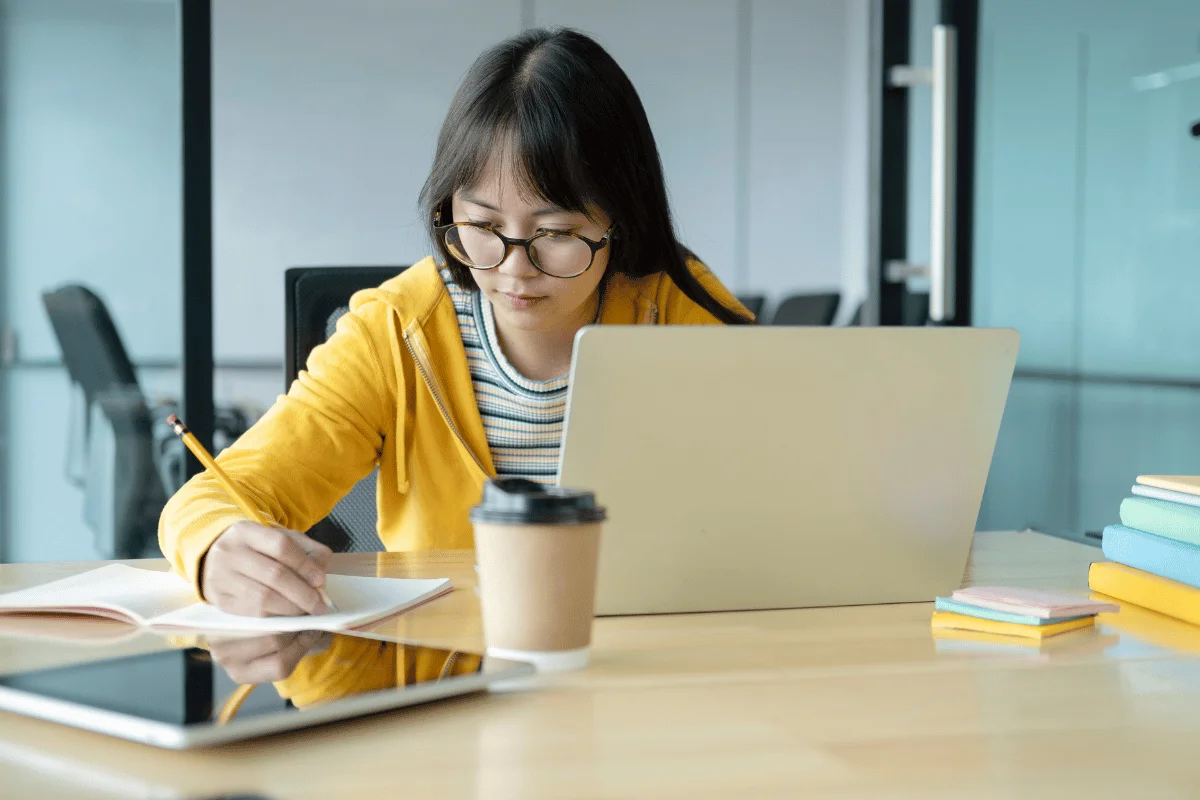 Young woman in a yellow hoodie writing notes during a study session.