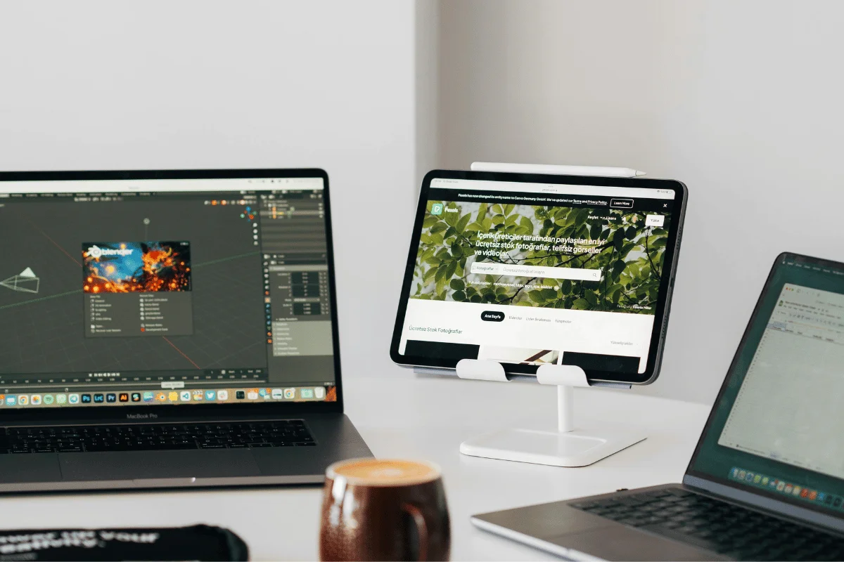 Multiple devices on a desk displaying creative software, stock images, and a text document with a coffee cup in view.