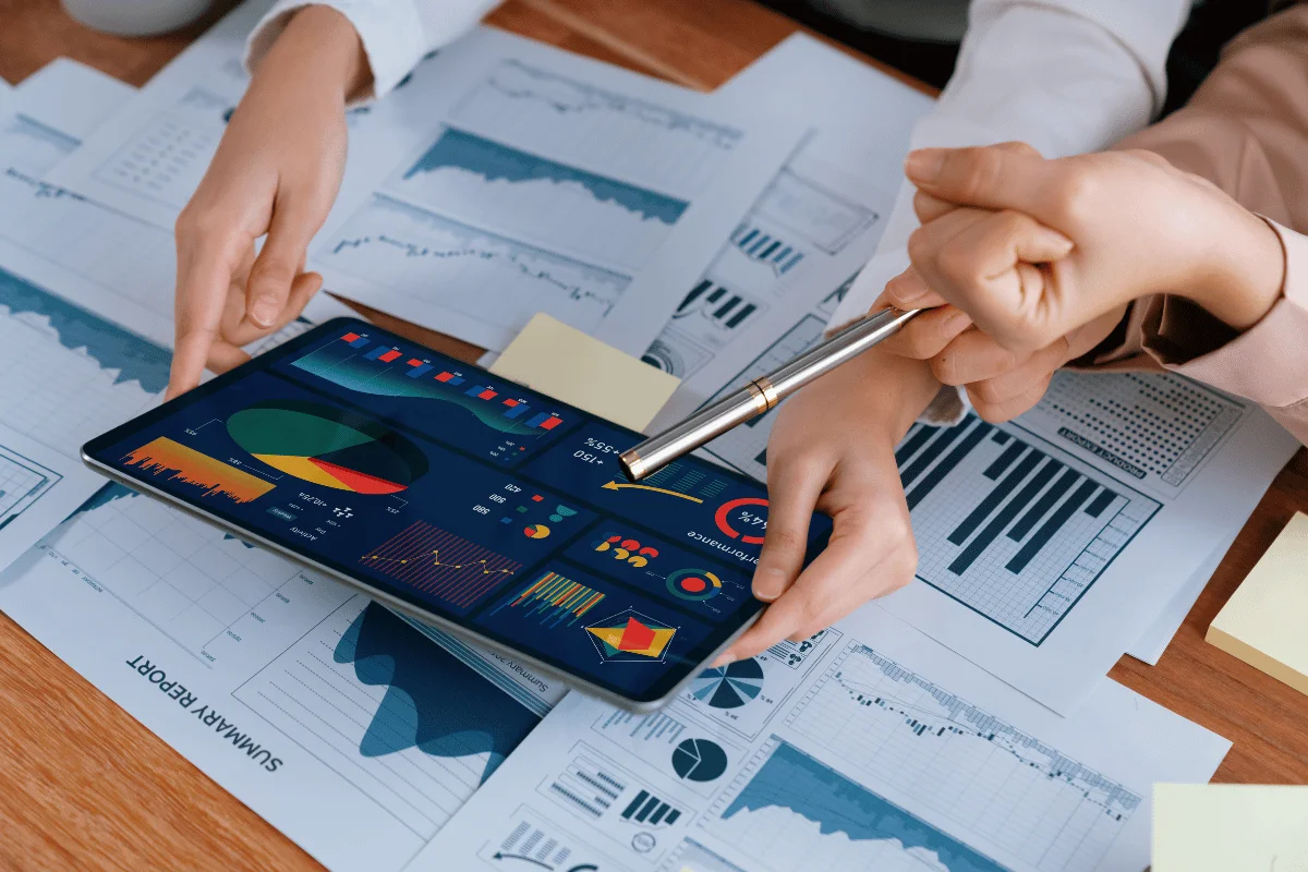 People analyzing charts on a tablet surrounded by financial reports.