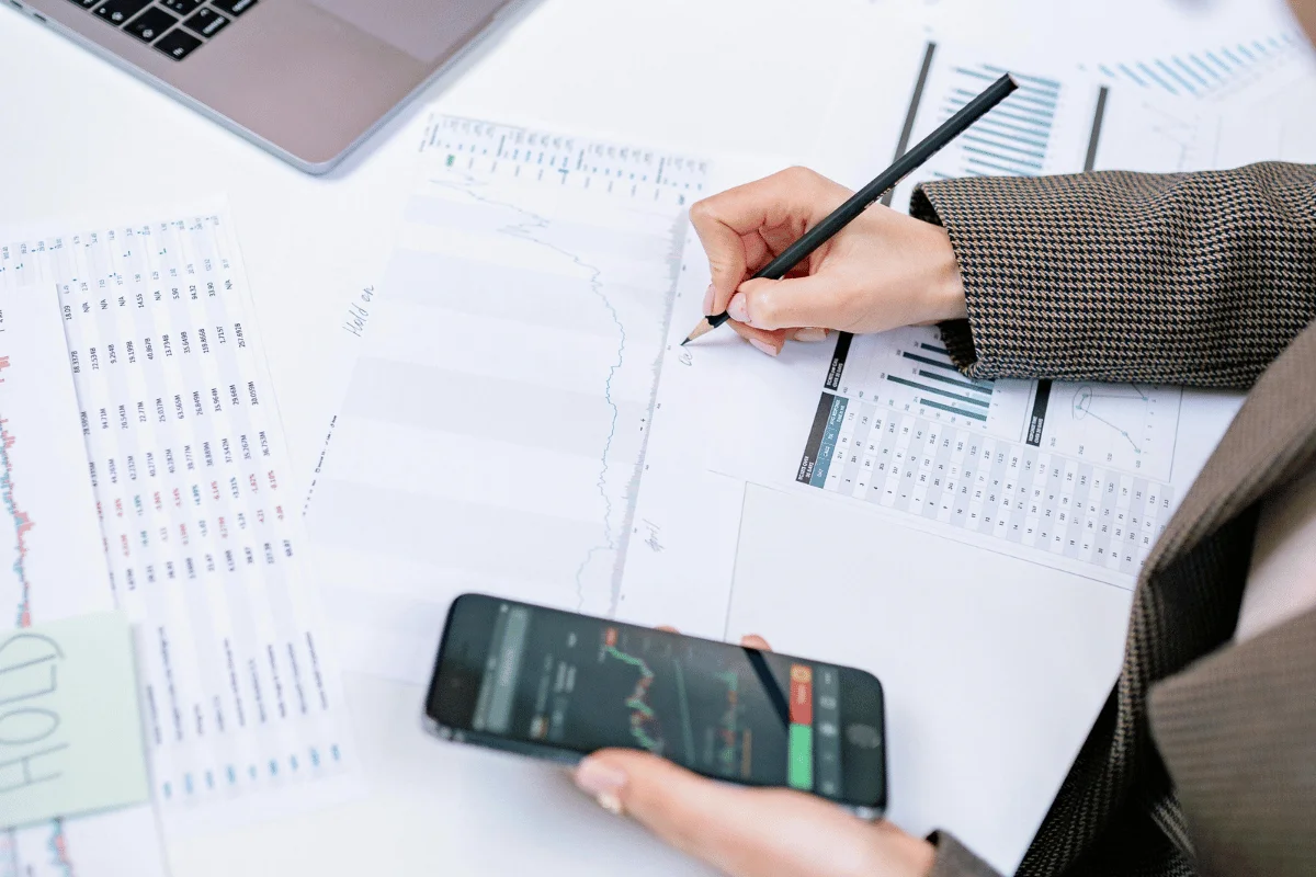 Close-up of financial market analysis on paper with smartphone data and handwritten notes.
