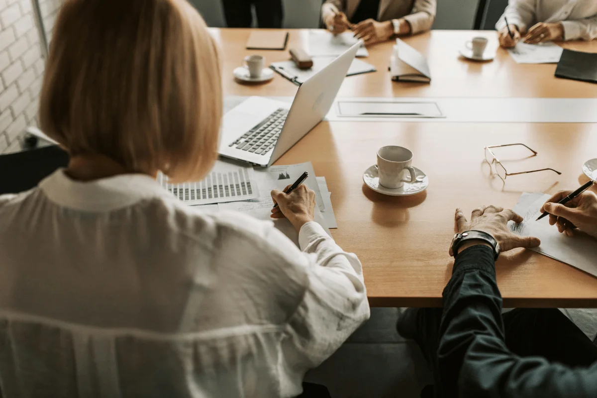 A group of professionals having a meeting, working on documents and laptops at a conference table.