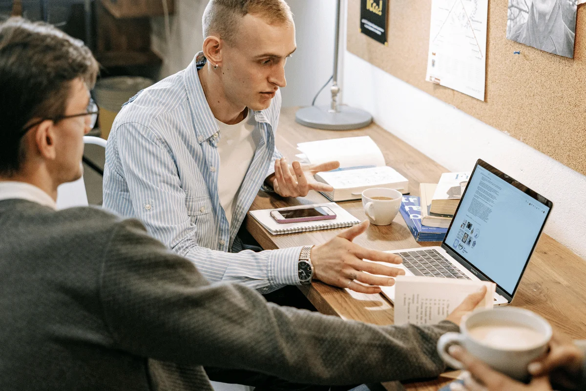 Team meeting with notes, coffee, and a laptop in a casual setting.